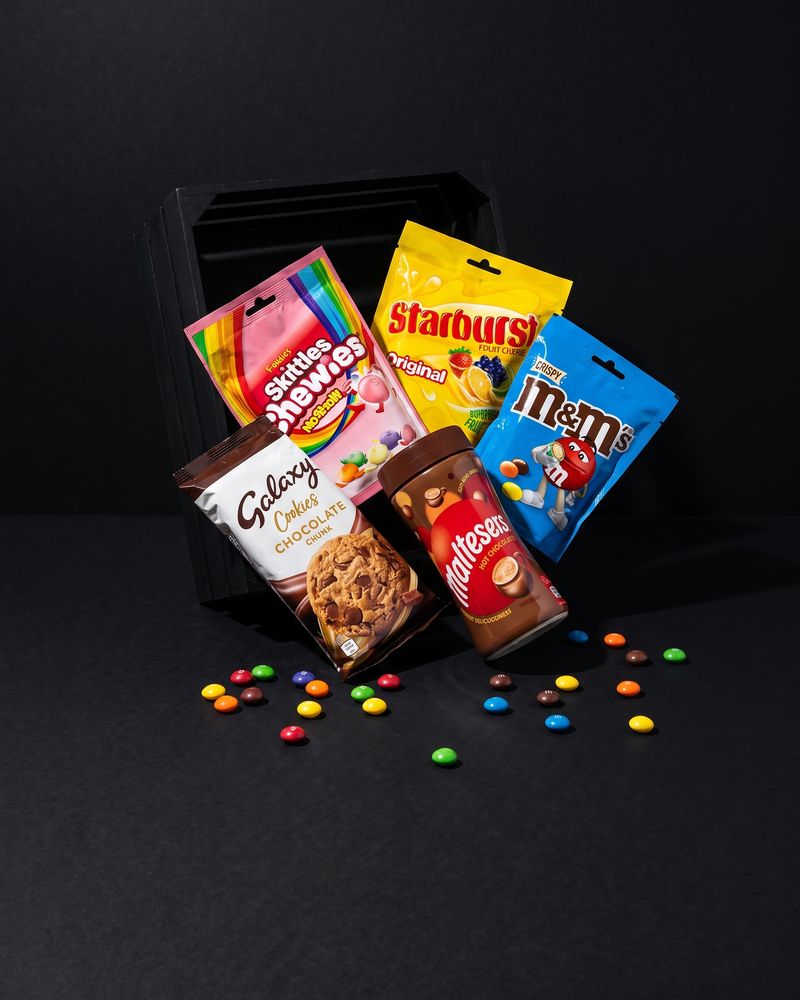 Chocolate countline bars cut to show their caramel layers beside candy-shelled chocolates, on a near-black background.