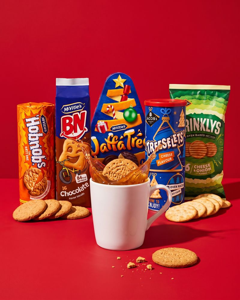 Stacked plain biscuit packets beside loose round biscuits on a bright red background.
