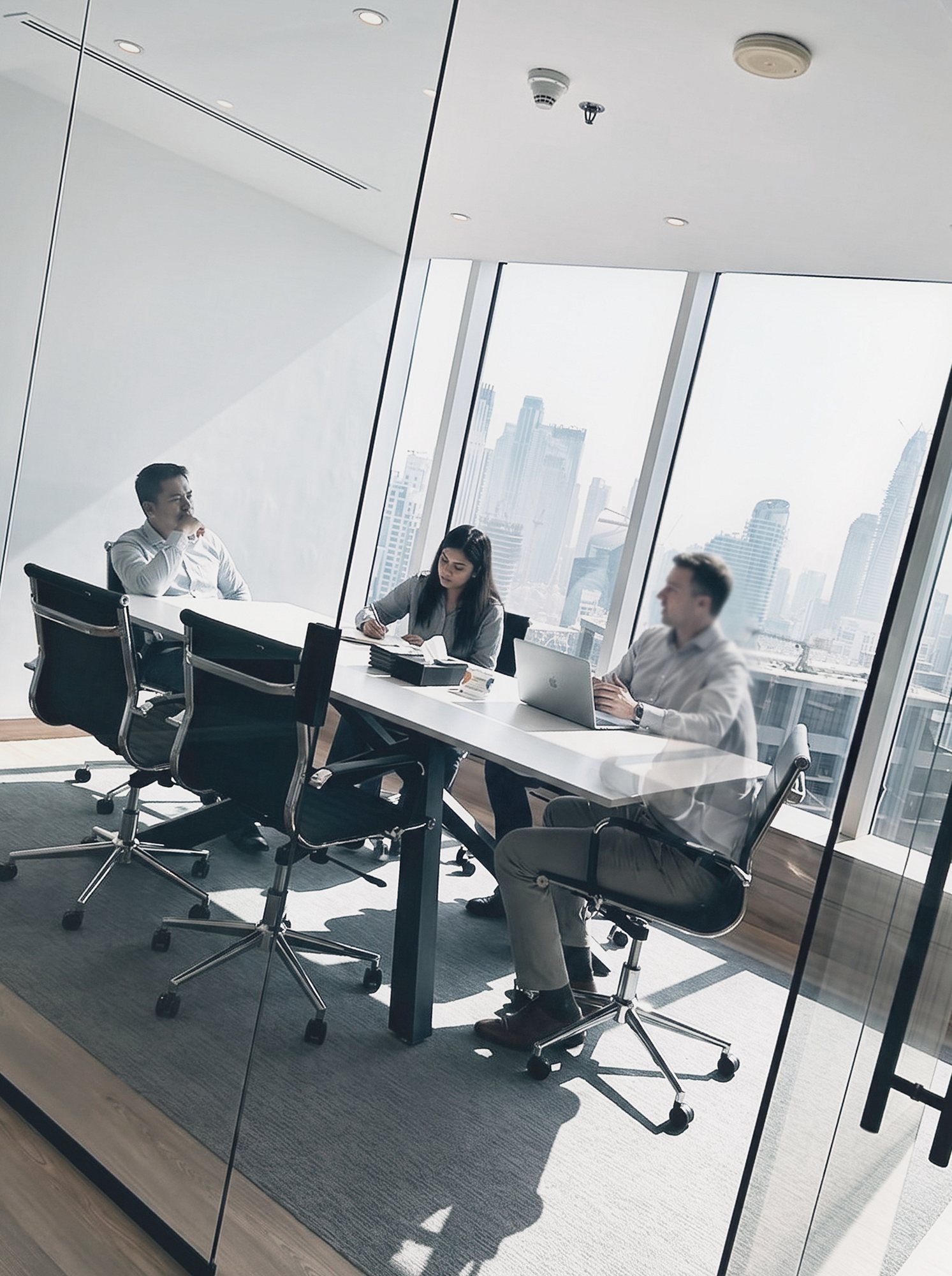 Three of the All About Brands team in a meeting room on our Dubai floor, the Business Bay skyline through the window behind them